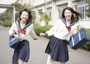 兩名身穿水手服、背著背包的女學生笑著在校園小徑上奔跑。
