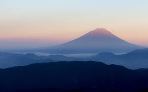 黎明時分的富士山，粉紅色和藍色的天空，霧氣繚繞的山巒層次。 — 日本 壁紙
