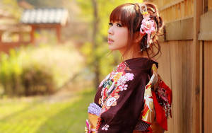 穿著花卉和服的女子在花園中靠著木柵欄，夕陽西下。