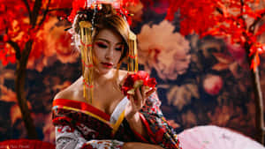 一位身穿紅金和服的藝妓在秋樹下手持紅花。