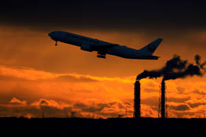 日本航空飛機在夕陽下起飛，工廠煙囪冒煙。