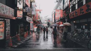 人們撐著傘走在雨中的日本街道上，兩旁有霓虹招牌和單車。