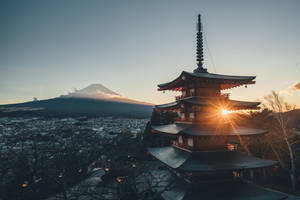 紅色寶塔背後有陽光散射，俯瞰富士山與城市日落景色。 — 日本 壁紙