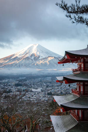 彎曲屋頂的紅色寺廟俯瞰著小鎮，背景是白雪覆蓋的富士山。 — 日本 壁紙
