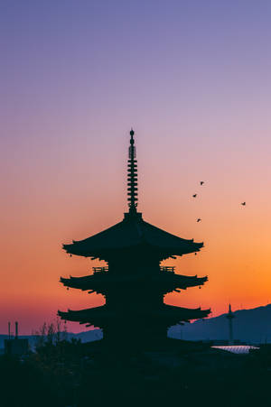 日落時分的寶塔剪影，鳥兒在橙色和紫色天空中飛翔