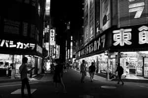 夜晚東京擁擠街道的黑白照片，有發光的招牌和行人。