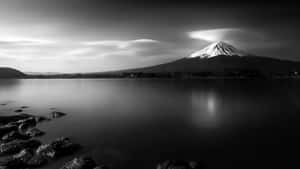 富士山在戲劇性雲層下的平靜湖泊倒影，黑白照片。