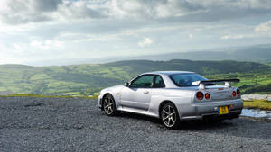 銀色日產Skyline GT-R停泊在風景如畫的山頂上，俯瞰綠色鄉村。 — 日產 Skyline GTR R33 壁紙