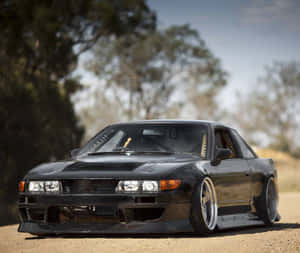 黑色改裝日產Skyline GT-R停放在泥路上，背景有樹木。