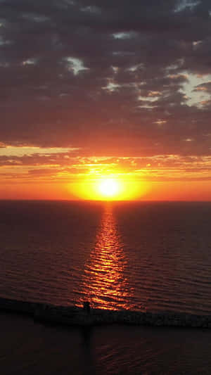 夕陽映照海洋，鮮豔的橙色和金色在平靜的水面上反射 — 手機 壁紙