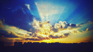 城市上空的夕陽，陽光穿透雲層，光芒四射。