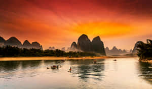 喀斯特山脈倒映在平靜的河流中，船隻在熾熱的日落天空下漂流。 — 向日葵田 壁紙