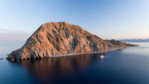 日落時分的崎嶇島嶼，平靜的海洋和附近停泊的遊艇。 — 加州 壁紙
