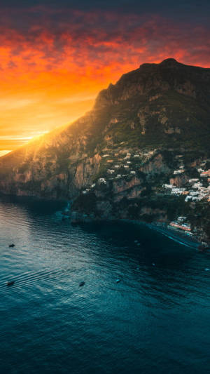 海岸村莊坐落在懸崖上，在深藍色大海之上，夕陽如火。 — 日落 壁紙