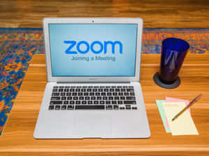 手提電腦顯示Zoom加入會議，木桌上有藍色玻璃杯和便利貼。