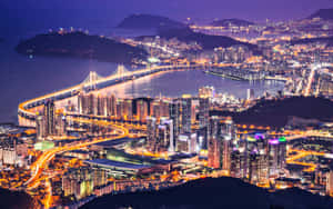 夜晚充滿活力的城市，水面上有燈光橋樑和高樓大廈。 — 2880x1800 壁紙