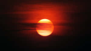 一顆發光的橙色太陽在紅色天空中落在暗雲後面。