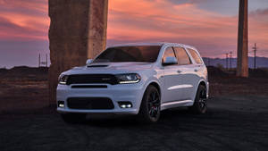白色Dodge Durango SRT SUV停泊在混凝土柱下的日落景色。 — 日落大道 壁紙