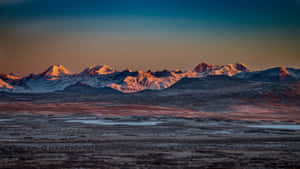 白雪覆蓋的山脈沐浴在金色夕陽光下，照耀著冰凍平原。