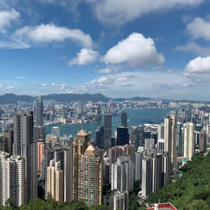 香港城市景觀，有摩天大樓、港口和山脈，在藍天白雲下。 — 天際線 壁紙