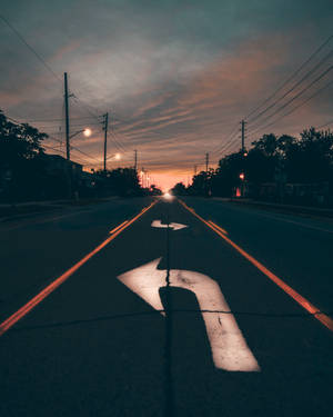 黃昏時分，一輛汽車在橙色的路燈和色彩繽紛的天空下行駛在寧靜的街道上。