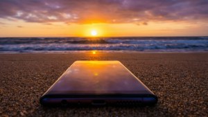 沙灘上的智能手機映照著夕陽在海浪之上