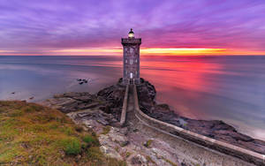 岩石海岸上的燈塔，色彩繽紛的夕陽，平靜的水面