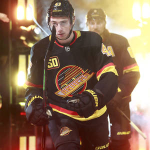 身穿 Canucks 球衣的冰球運動員走過明亮的場館燈光。