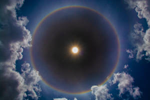 太陽帶有彩虹光環和白雲在藍天中