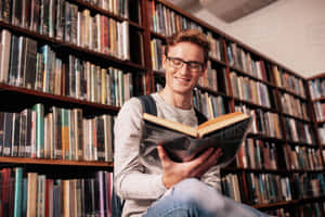戴眼鏡的年輕男子在圖書館閱讀時微笑。