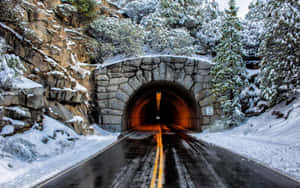 一條積雪的山路通往一個帶有溫暖室內燈光的石隧道。 — 道路 壁紙
