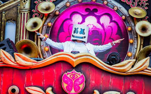 DJ Marshmello 戴著他的標誌性面具，站在一個色彩繽紛的音樂會舞台上，配有黃銅喇叭和粉紅色燈光。