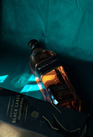 Johnnie Walker Black Label威士忌酒瓶和盒子放在青綠色布料上，帶有戲劇性的燈光。 — 小米Pad 7S Pro 12.5 壁紙