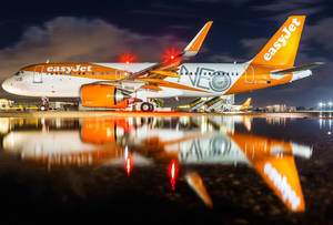 橙色和白色的易捷航空飛機夜間停放，在濕滑跑道上反射。
