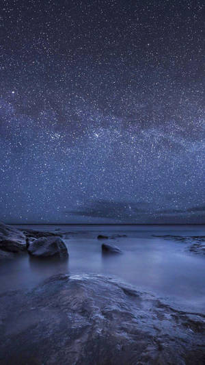 平靜海洋上的星空夜空，光滑流動的水和暗色岩石。