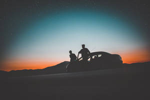 兩人在沙漠山頂的汽車旁，暮色下星空璀璨