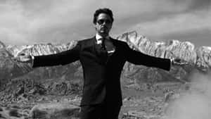 穿著西裝和太陽眼鏡的男人在沙漠山景中張開雙臂站立。