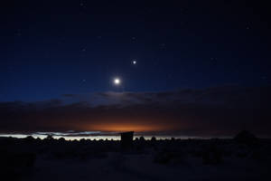 夜晚的雪沙漠景觀，有星星、月亮和橙色地平線光芒。