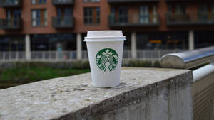 一個Starbucks咖啡杯放在混凝土欄杆上，背景是城市建築。