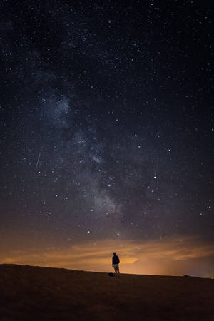 一個人的剪影站在沙漠沙丘上，在銀河和流星點綴的星空下。