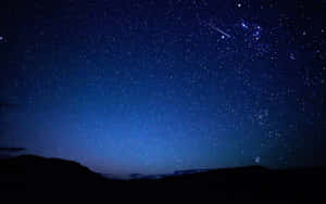 一顆流星劃過黑暗山丘上方的繁星夜空。 — 星星 壁紙