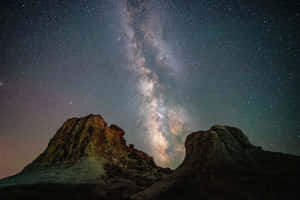 銀河系在繁星點點的夜空下，拱起於沙漠岩石地貌之上。 — 星星 壁紙