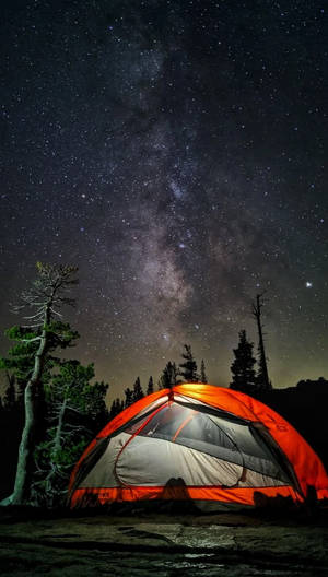 在繁星點點的夜空下，一個明亮的橙色帳篷，上方可見銀河。
