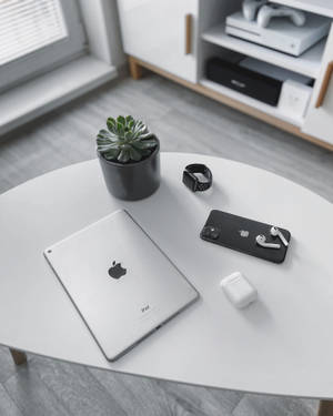 白色桌子上有iPad、電話、智能手錶、耳機和多肉植物，在現代房間中。