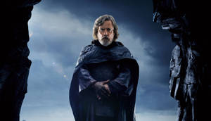 Luke Skywalker 身穿深色長袍，站在暴風雨天空下的岩石拱門中。