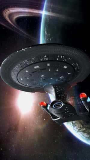 星艦企業號在深空中環繞一顆帶環行星運行，背後有一顆明亮的星星閃耀。