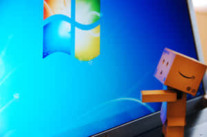 帶有亞馬遜標誌的紙板Danbo在顯示Windows 7桌面的筆記本電腦旁邊微笑。