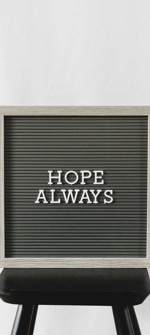 一個黑色字母板，上面用白色字母寫著HOPE ALWAYS，放在一個黑色凳子上。