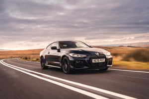 黑色BMW雙門轎跑車在日落時分沿著彎曲的道路穿過金色田野飛馳。