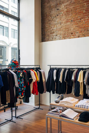 在極簡城市精品店中，服裝架和折疊服裝，配有裸露磚牆和大窗戶。